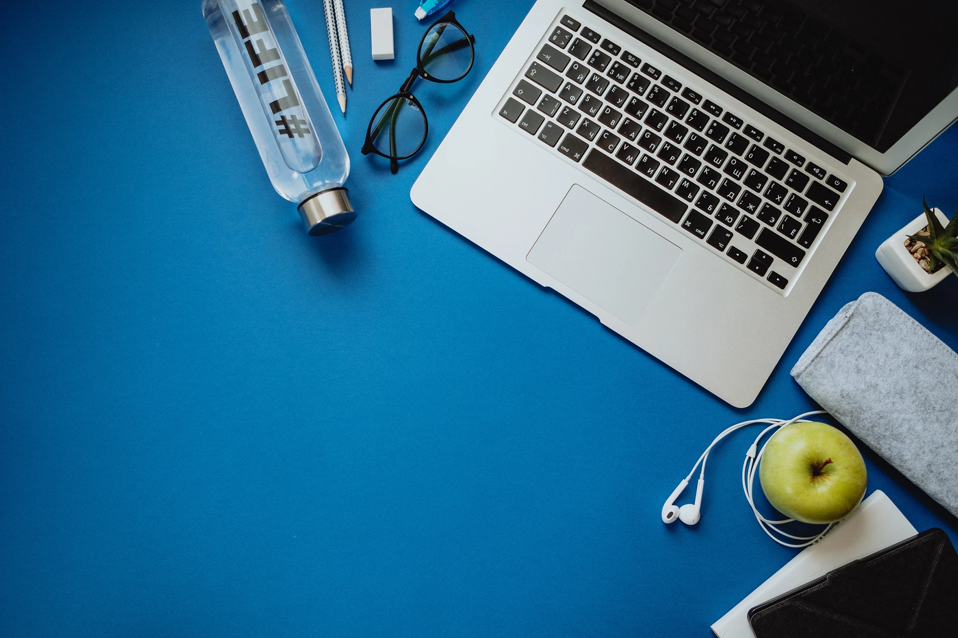 Workspace for healthy person with laptop, pencils, water, apple, phone, glasses, headphones on a blue background. Top view, flat lay Arbeitsplatz gesunde Person mit Laptop, Stiften, Wasser, Apfel, Telefon, Brille, Kopfhörern auf einem blauen Hintergrund. Draufsicht